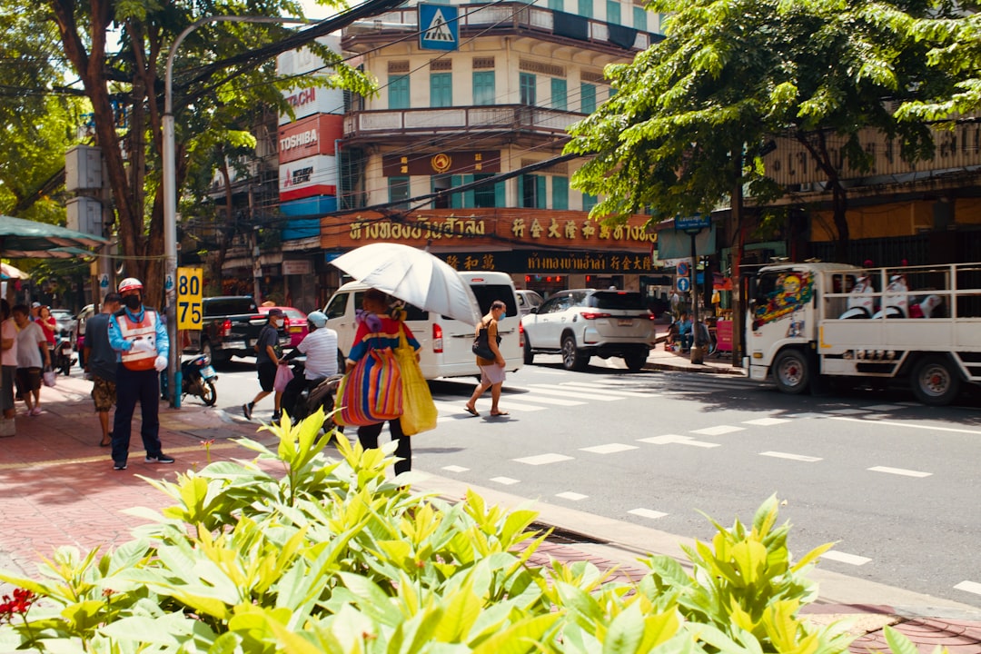 Busy Thai street scene with pedestrians, tropical plants, and colonial-style buildings with Thai signage