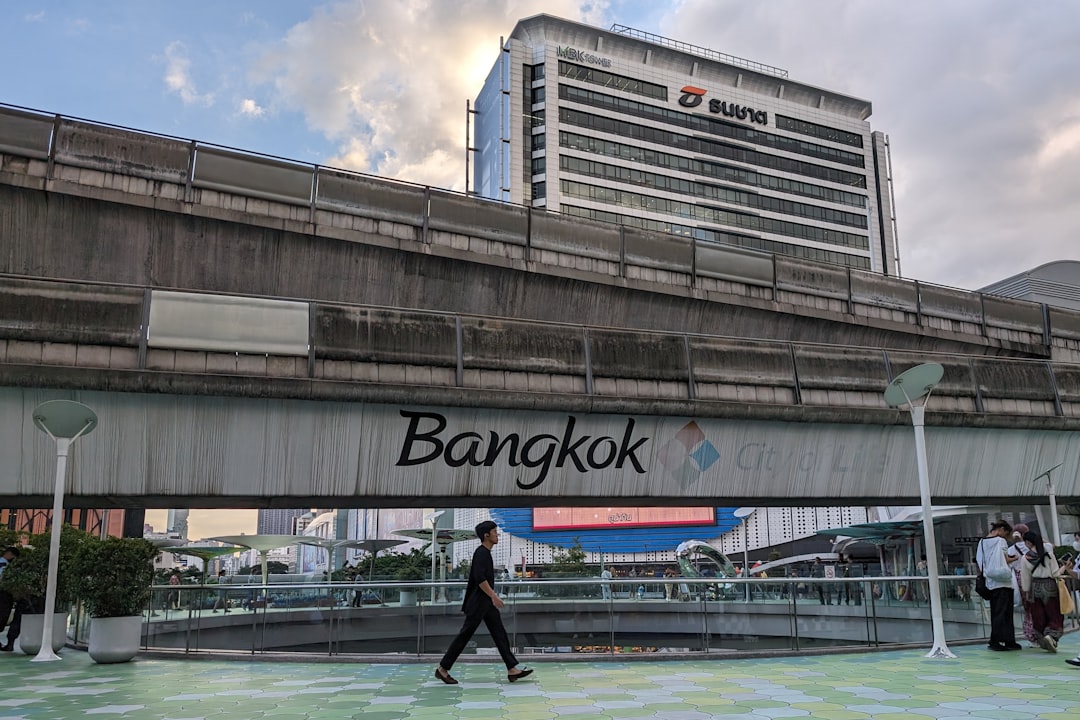Bangkok BTS Skytrain station platform with modern office building and pedestrians