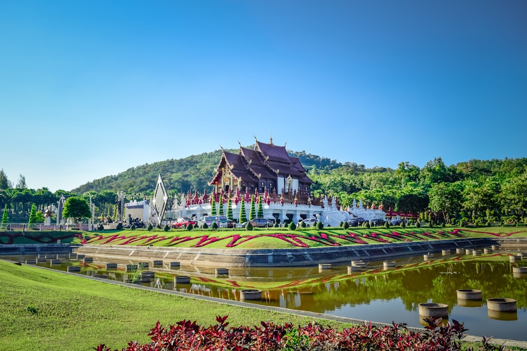 Purple Thai temple with white base beside river and colorful flower gardens under clear sky