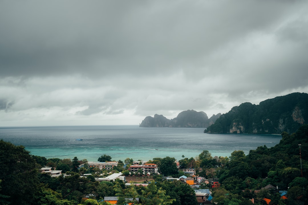 Tropical coastal village with limestone cliffs and turquoise waters under dramatic cloudy sky