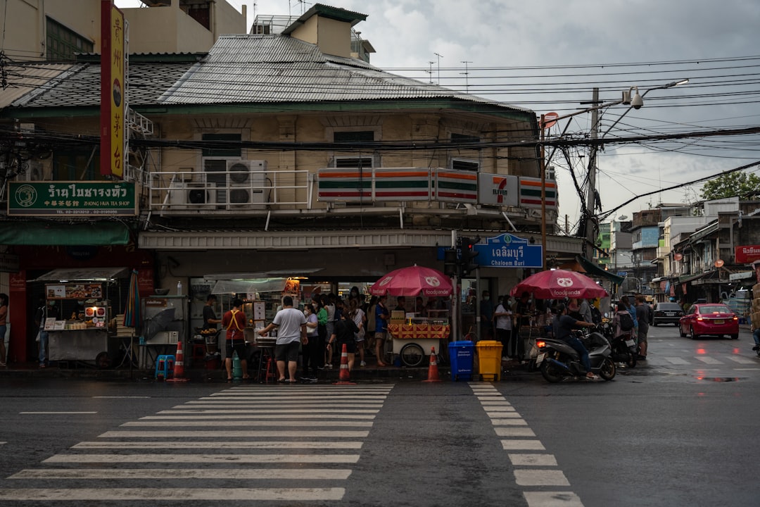 Street vendors with red umbrellas at a busy Bangkok intersection near Chaloem Buri station