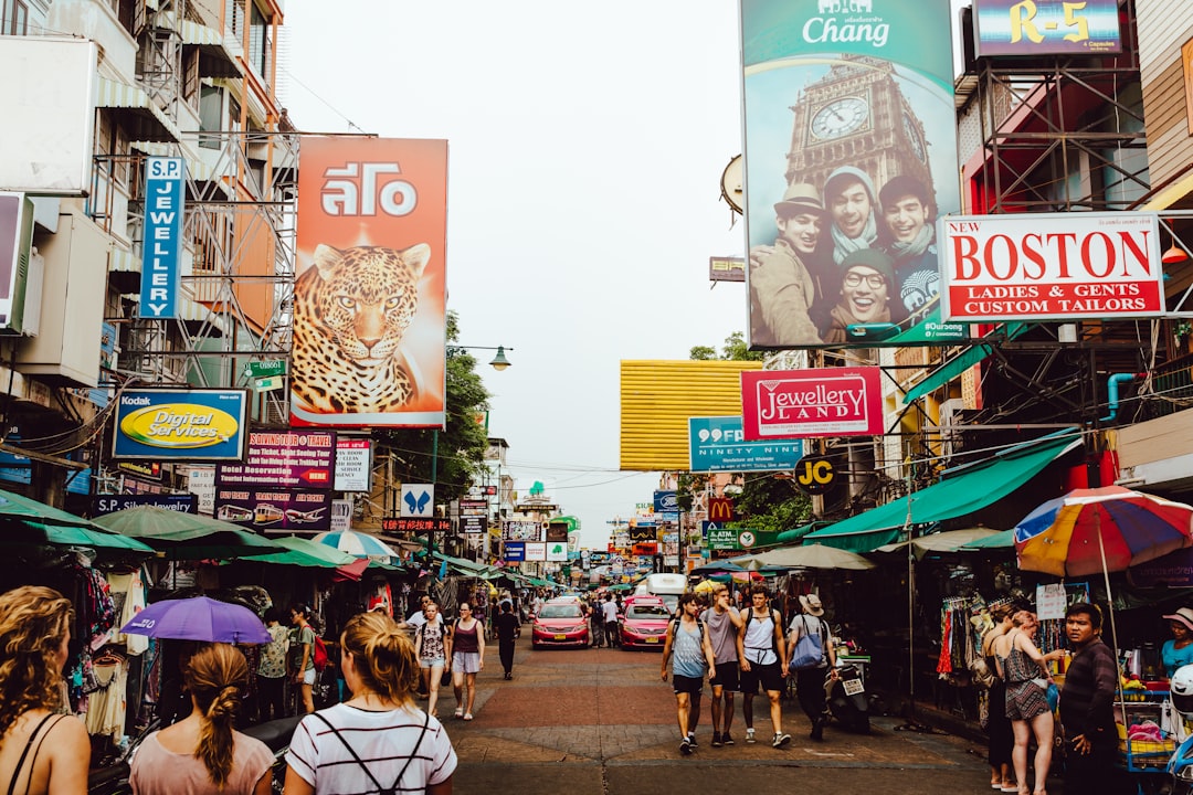 Busy street market in Bangkok with colorful umbrellas, shop signs, and crowds of pedestrians