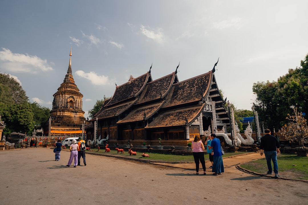Traditional Thai temple with golden stupa and ornate wooden structures surrounded by visitors