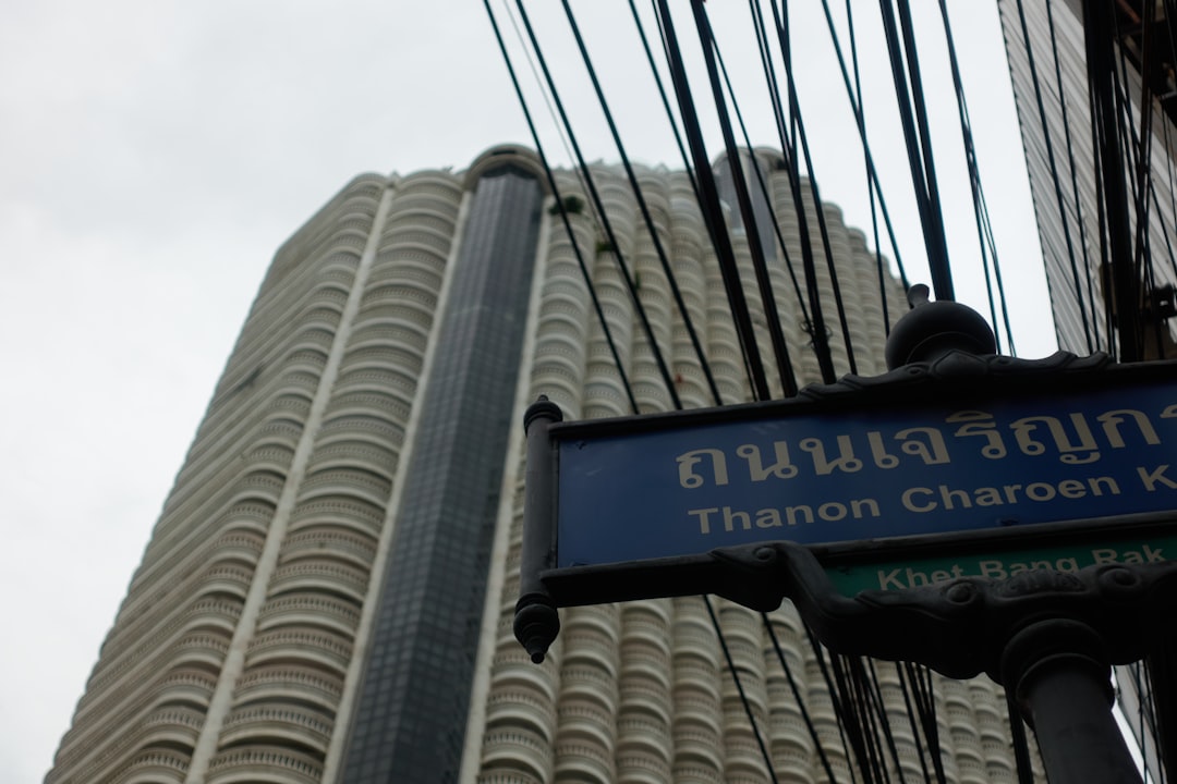Bangkok street sign showing Thanon Charoen with modern high-rise building in background